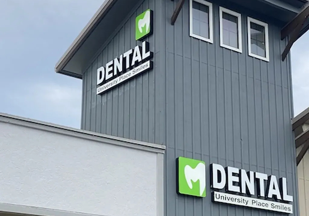 Exterior of "University Place Smiles Dental" building with signage featuring a green tooth logo - Dentist University Place WA Exterior of "University Place Smiles Dental" building with signage featuring a green tooth logo - Dentist University Place WA
