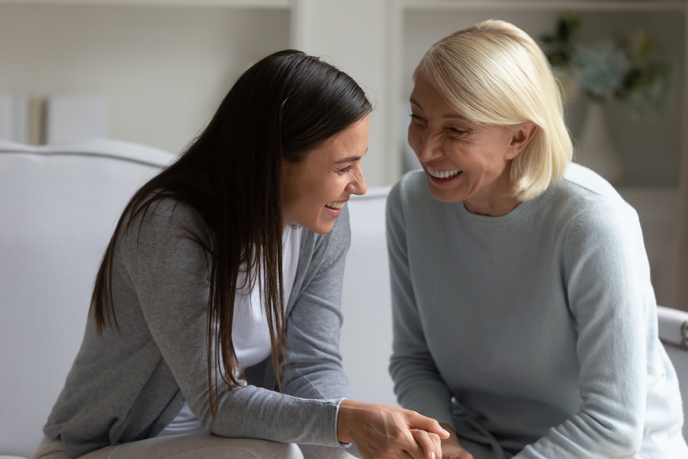 Overjoyed senior mother and grown up adult daughter sit on couch - University Place Cosmetic Dentistry