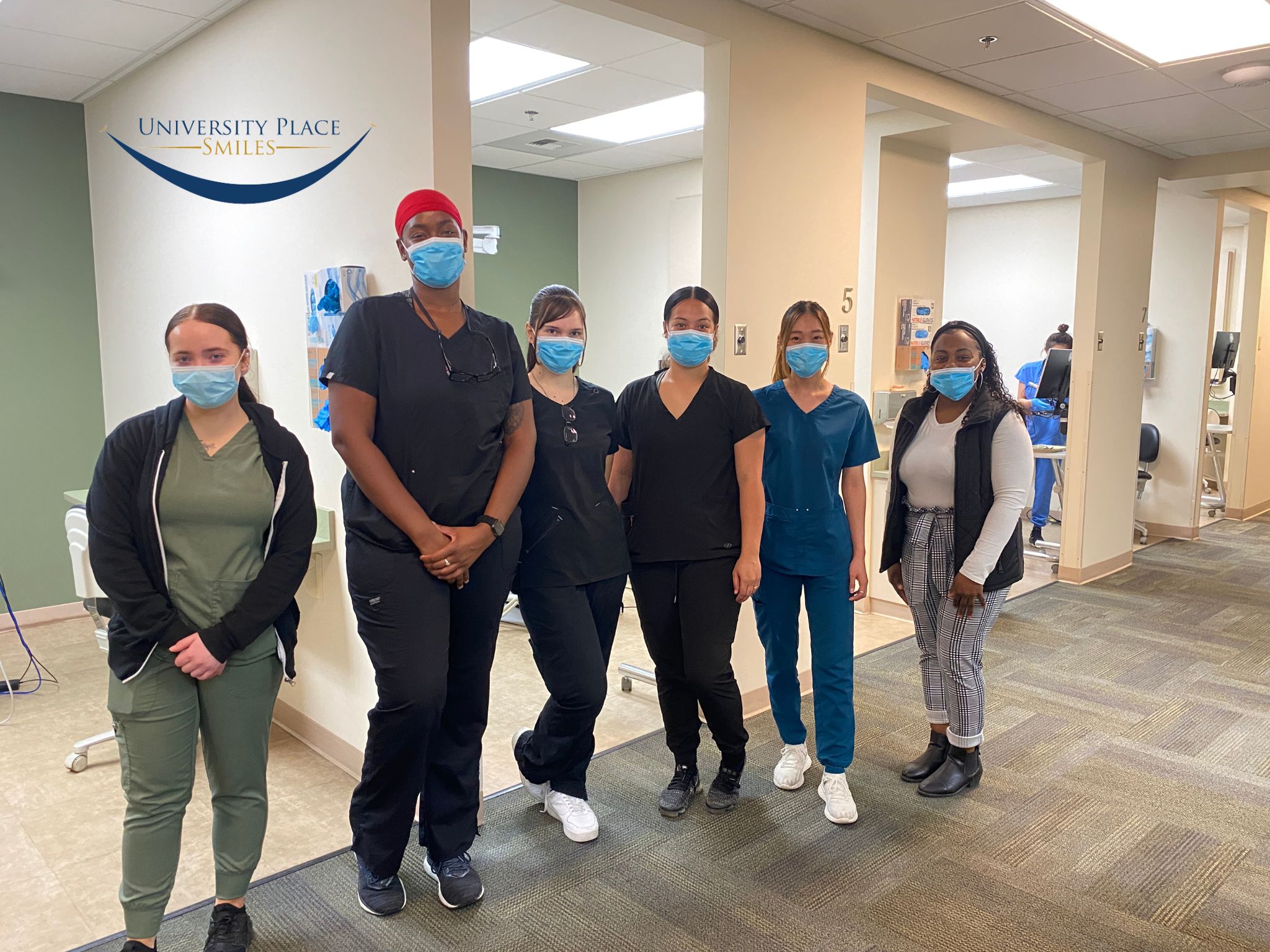 A group of six dental staff members at University Place Smiles, wearing masks and standing together in a clinic hallway - Dentist University Place WA A group of six dental staff members at University Place Smiles, wearing masks and standing together in a clinic hallway - Dentist University Place WA