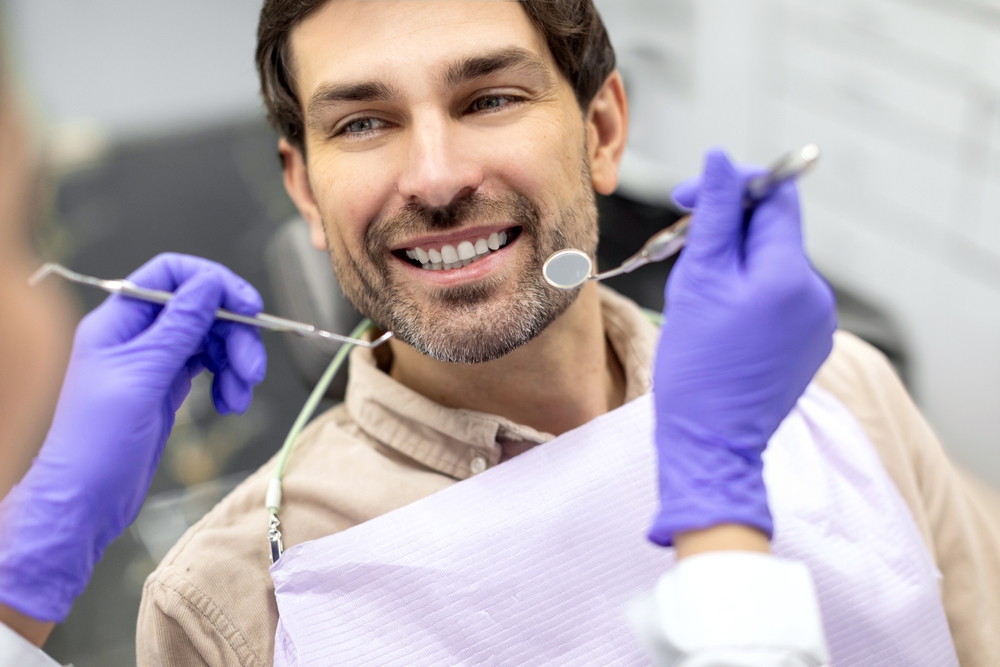 A smiling man in a dental chair receiving an examination from a dental professional wearing purple gloves - Dentist University Place WA A smiling man in a dental chair receiving an examination from a dental professional wearing purple gloves - Dentist University Place WA